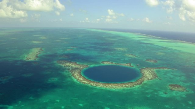 Aerial view of yacht next to large marine sinkhole against sky, scenic view of seascape on sunny day while drone moving backward - Great Blue Hole, Belize