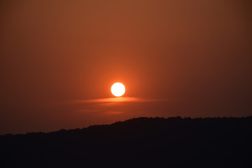 Orange sun setting on black hill silhouette, illuminated cloud, Hangzhou, China