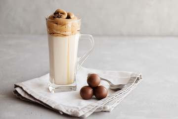 Cold dalgon milk and coffee drink in a glass on a linen napkin and next to chocolates. Place for text