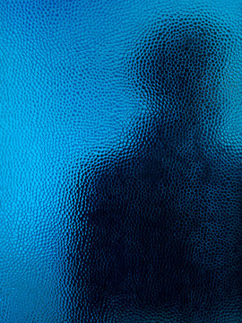 Man in black hoodie behind closed door seen through glass.