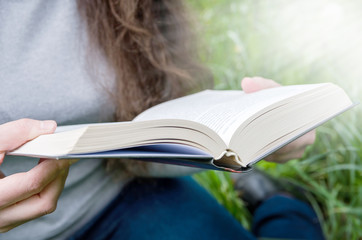 girl reads a book on a background of green grass. Close-up. Image is tinted.