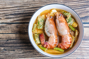 Close-up of two shrimps with vegetable sour curry Thai soup with Acacia Pennata omelet and shrimps in a white bowl on a wooden table. The idea of healthy herbal ingredient food and cooking stay home.