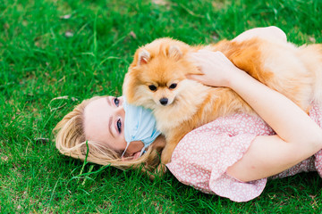 Young woman and red spitz with a medical mask on her face on nature on a spring day. Coronavirus pandemic