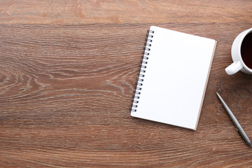 Wood office desk table with blank notebook with pen and cup of coffee. Top view with copy space, flat lay.