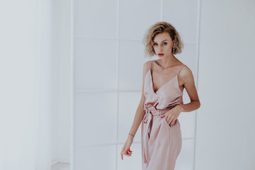 Beautiful fashionable blonde woman in pink silk dress on a white background