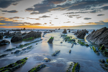 long exposured coast with rocks and sunset at the back