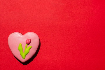 Handmade gingerbread cookie in the shape of heart and with painted by icing tulip on the bright red background. Copy space. Top view.