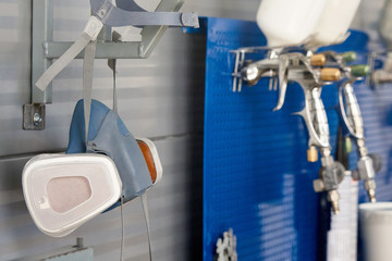 Professional respirator in auto repair shop with spray guns on background