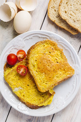 French toast, fried in eggs, lies in a plate on a light wooden rustic table