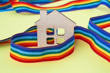mini toy wooden house and lgbt rainbow ribbbon on yellow background