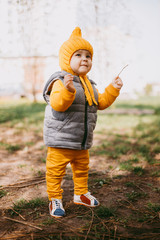 Stylish little one-year-old boy in a yellow hat, yellow pants and a gray jelly