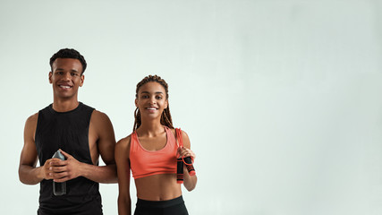 Healthy and positive. Young smiling african couple in sportswear looking at camera while standing against grey backgroun