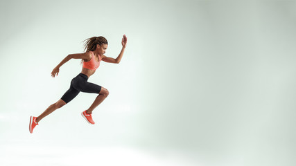 Fototapeta na wymiar Never give up. Full length of young african woman with perfect body in sports clothing jumping in studio against grey background