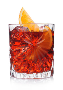 Negroni Cocktail in crystal glass with ice cubes and orange slice on white background with reflection.