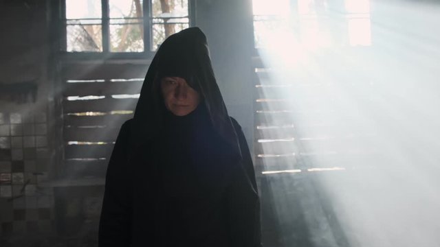woman Psychic in black mantle with contempt on face looking at camera walking in abandoned building.