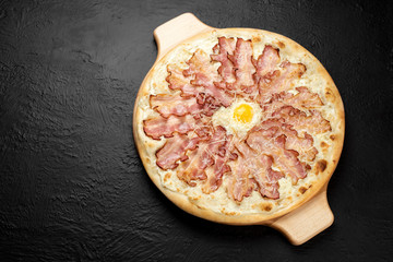 CARBONARA pizza on a black background, cream-based with mozzarella, bacon, Parmesan, garlic and egg