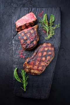 Gegrilltes dry aged Wagyu Roastbeef Steak mit Salat und Kräutern als Draufsicht auf einem rustikalen verkohlten Holz Board