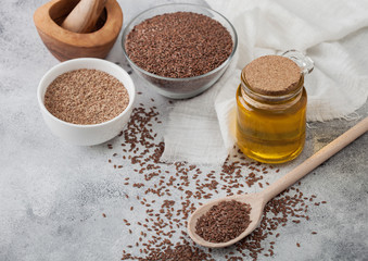 Bowl of raw natural organic linseed flax-seed with spoon and glass jar oil on light table background with linen cloth.
