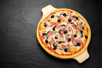 Milanese pizza on a black background, tomato-based with mozzarella, ham, mushrooms, onions and olives