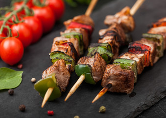Grilled pork and chicken kebab with paprika on stone chopping board with salt, pepper and tomatoes on black background.