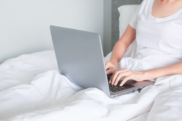 Fototapeta premium A woman using a laptop to work on the bed, work from home concept.