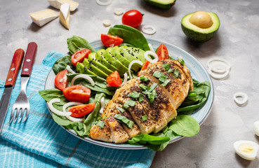Grilled chicken breast and avocado salad with spinach and cherry tomatoes on concrete background. Healthy food, ketogenic diet