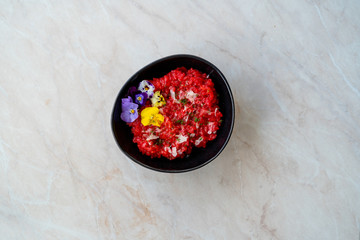 Beetroot Risotto with Edible Flowers and Parmesan Cheese made with Organic Beet in Black Ceramic Bowl.