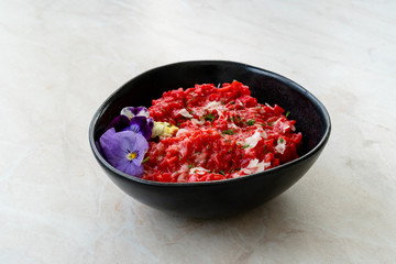Beetroot Risotto with Edible Flowers and Parmesan Cheese made with Organic Beet in Black Ceramic Bowl.