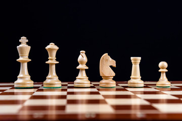 white chess pieces stand in a row on a chessboard on a black background