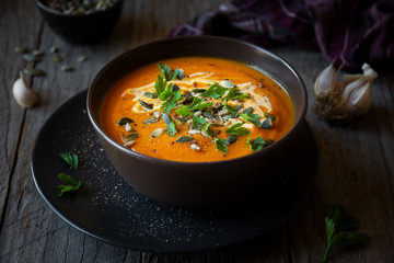 Pumpkin soup with cream, parsley and pumpkin seeds on dark background
