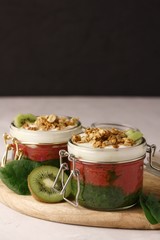Spinach and kiwi smoothies and raspberry smoothies in glass jars with yogurt and granola on a wooden board