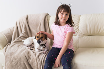 Child girl with cute dog jack russell terrier on the couch. Pets , children and home concept.