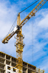 Fototapeta na wymiar One yellow high crane against a house and sky during the construction phase. Industry concept for low-income young families. Mortgage, business, real estate loan.