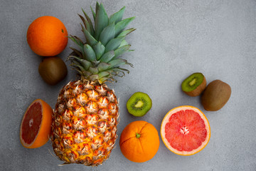 Ripe pineapple and other tropical fruit - orange, kiwi, grapefruit on grey background