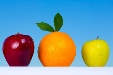 Two apples and an orange together with the blue sky in the background that serves as contrasting color.