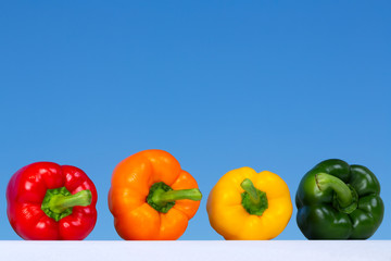 The four colors of Pepper Bells: red, orange yellow and green, complementary colors, laying over a contrasting blue color from the sky as background.