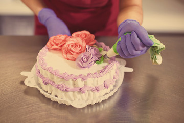Obraz na płótnie Canvas Pastry chef decorates the cake with flowers from the cream. The cream is squeezed out of the pastry bag through a special nozzle