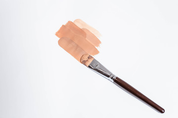 Beige liquid creamy foundation stroke smear and make-up brush isolated on white background, top view. BB cream or CC cream sample smudge, vertical.