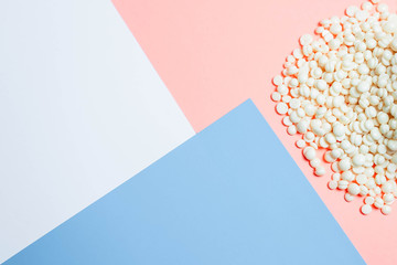Wax for depilation of white pearl color and wooden stick spatula on pink and blue background....
