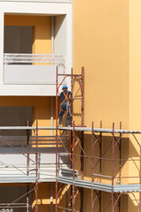 Worker with Blue Hardhat at Work on a Scaffold in a Building Site for the Construction of a Building