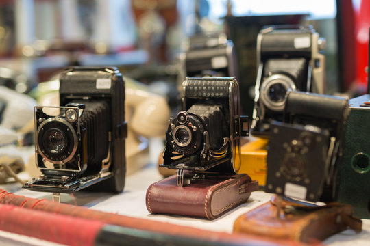 Antique Black Folding Cameras with Bellows on a Shelf