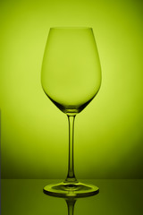 The crystal glass stands on the reflecting surface on a lime background. studio photo. product. Beautiful shadow from wine glass. macro photo