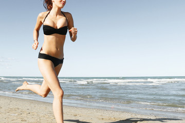 Fototapeta na wymiar beautiful woman in bikini running on beach midsection close-up .