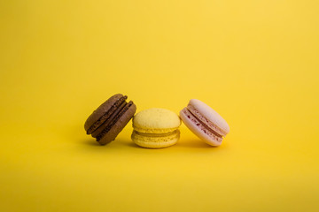 Set of three macarons on a yellow background with copy space. Brown, yellow and pink macaroni are in a row.