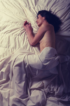 Conceptual image of a woman sad and lone on a bed under a sheet