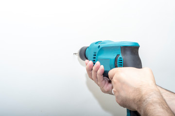 Men's hands hold a drill on a light background