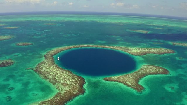 Aerial shot of yacht in famous marine sinkhole against sky, drone moving forward over seascape on sunny day - Great Blue Hole, Belize