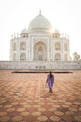 Woman wearing a blue sari looking at the Taj Mahal at sunrise