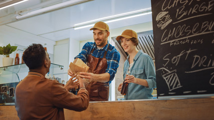Obraz premium Food Truck Employee Hands Out Burger and Cold Drink to Happy Young Hipster Customer. Commercial Truck Selling Street Food in Modern Cool Neighbourhood.