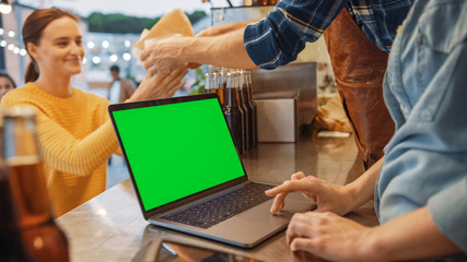 Laptop Computer with Green Screen Mock Up Screen is Placed on a Counter at a Street Food Truck or Kiosk that Sells Burgers and Drinks. Happy Customers Receive Their Orders.